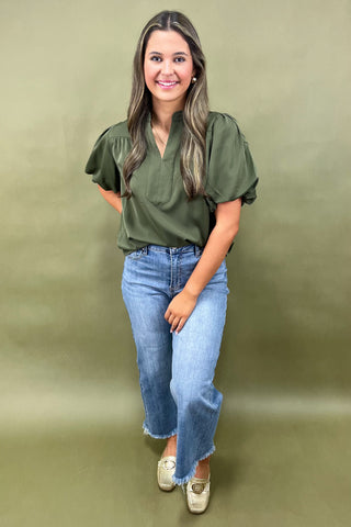 Olive green puff sleeve blouse with split neckline styled with light wash wide leg frayed hem jeans and gold loafers.