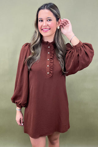 Woman wearing a brown dress with long sleeves against a green background