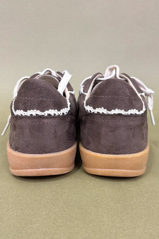 Pair of brown suede shoes with white laces on a beige background