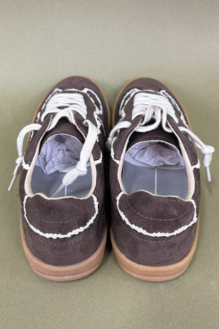 Pair of brown sneakers with white laces on a light green background