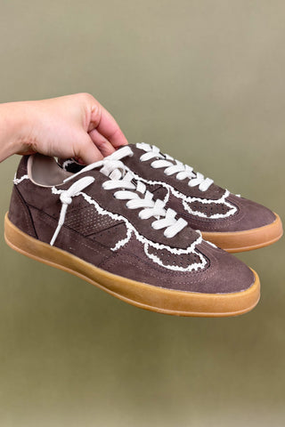 Brown sneakers with white laces held by a hand against a green background