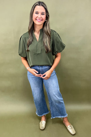 Olive green puff sleeve blouse with split neckline styled with light wash wide leg frayed hem jeans and gold loafers.