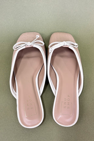 Pair of beige sandals with white straps on a green background