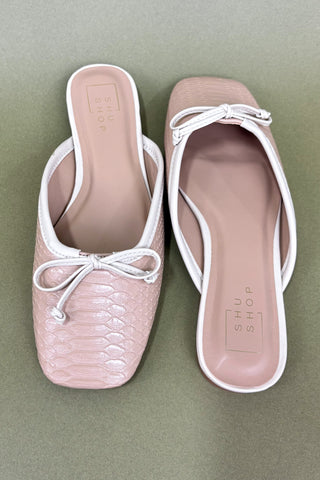 Pair of pink slipper shoes with white bows on a green background