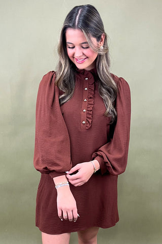Woman wearing a brown dress with long sleeves against a green background