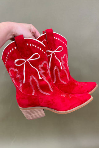 Red cowboy boots with white embroidery and bows held against a gray background