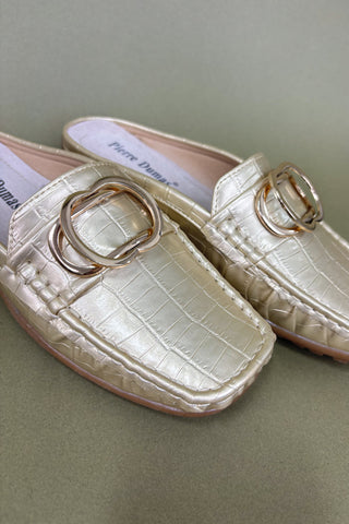 Pair of cream-colored loafers with gold rings on a light green background