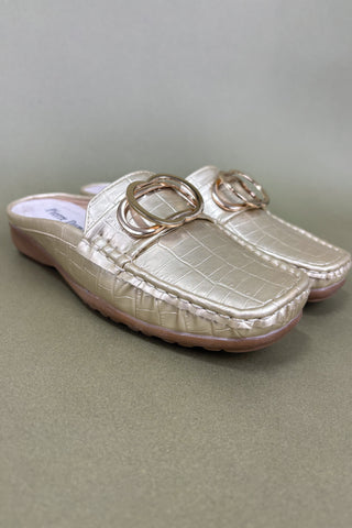 Pair of cream-colored loafers with gold rings on a light green background