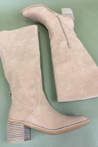 Pair of beige knee-high boots with transparent heel on a green background
