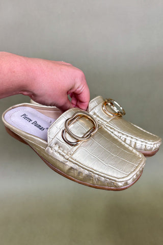 Gold slipper with a decorative buckle held by a hand against a neutral background