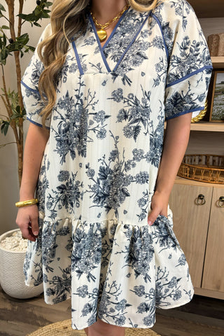 Woman wearing a white dress with blue floral patterns indoors.