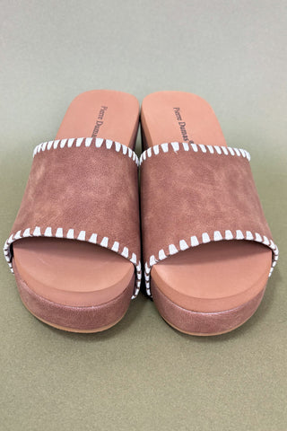 Pair of brown sandals with white trim on a green background