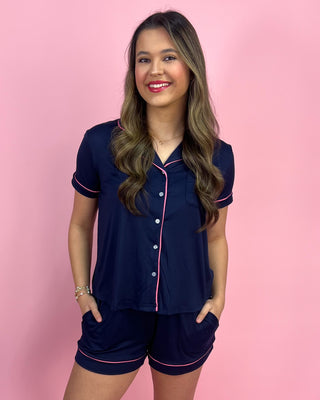 Woman wearing a navy pajama set with pink piping against a pink background