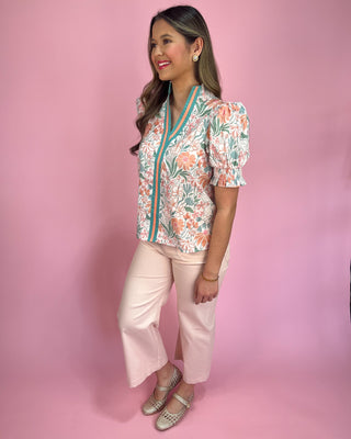 Woman wearing a floral blouse and pink pants against a pink background