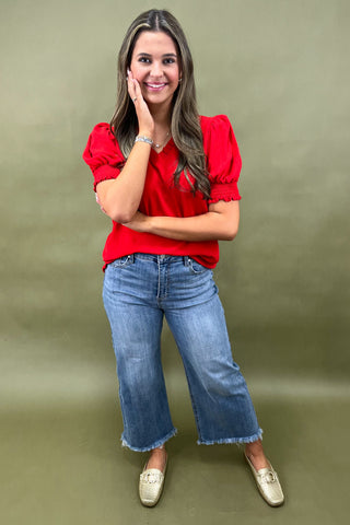 Red puff sleeve blouse with v-neckline styled with light wash wide leg frayed hem jeans and gold loafers.