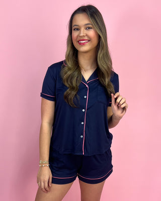 Woman wearing a navy pajama set with pink piping against a pink background