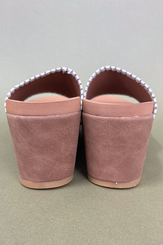 Pair of pink slippers with decorative trim on a beige background