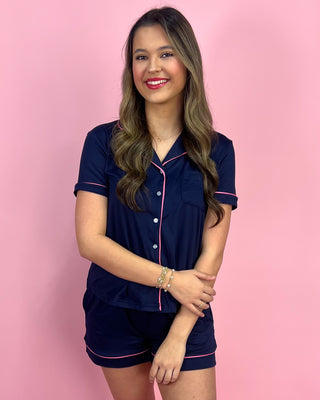 Woman wearing a navy pajama set with pink piping against a pink background