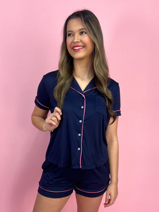 Woman wearing a navy pajama set with pink piping against a pink background