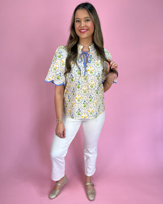 Woman wearing a floral blouse and white pants against a pink background