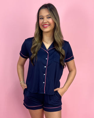 Woman wearing a navy pajama set with pink piping against a pink background
