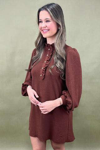 Woman wearing a brown dress with ruffled details on a green background