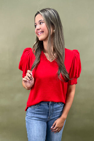 Red puff sleeve blouse with v-neckline styled with light wash wide leg frayed hem jeans and gold loafers.