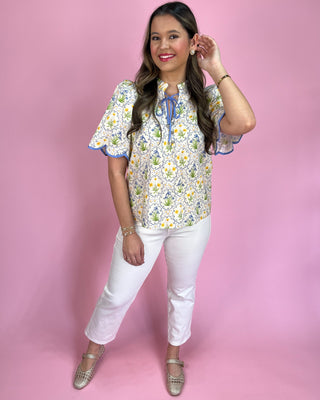 Woman wearing a floral blouse and white pants against a pink background