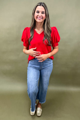 Red puff sleeve blouse with v-neckline styled with light wash wide leg frayed hem jeans and gold loafers.