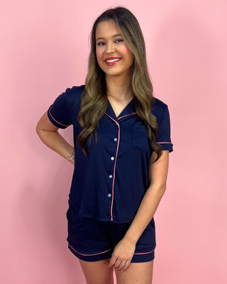 Woman wearing a navy pajama set with pink piping on a pink background