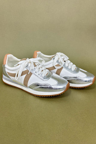 Pair of silver and white sneakers with brown soles on a green background