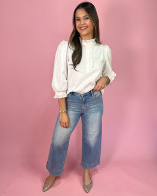 Woman wearing a white blouse and blue jeans against a pink background