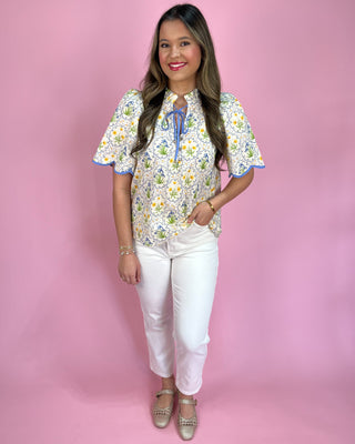 Woman wearing a floral blouse and white pants against a pink background