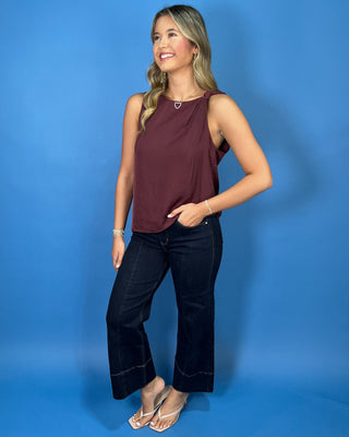 Wine sleeveless top with a soft draped silhouette, rounded neckline, and chic knotted shoulder detail.