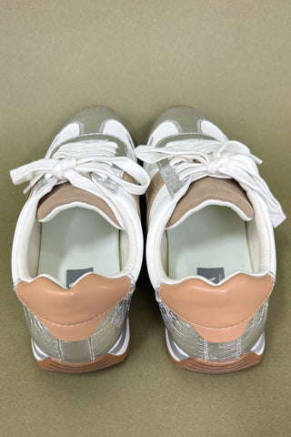 Pair of white sneakers with tan soles on a beige background