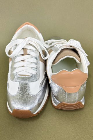 Pair of white sneakers with brown soles on a green background