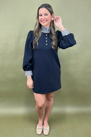 Woman wearing a navy dress with striped cuffs against a green background