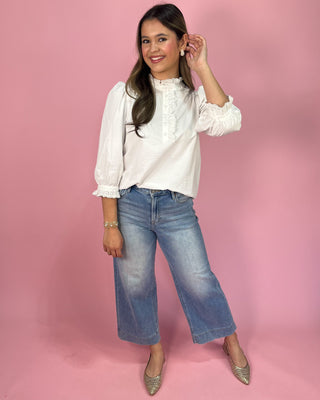 Woman wearing a white blouse and blue jeans against a pink background