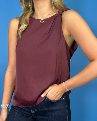 Wine sleeveless top with a soft draped silhouette, rounded neckline, and chic knotted shoulder detail.