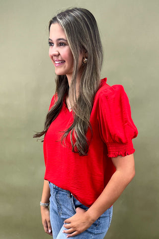 Red puff sleeve blouse with v-neckline styled with light wash wide leg frayed hem jeans and gold loafers.