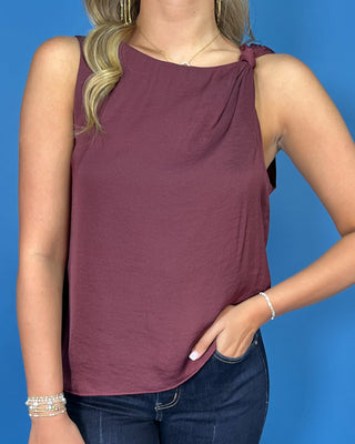 Wine sleeveless top with a soft draped silhouette, rounded neckline, and chic knotted shoulder detail.