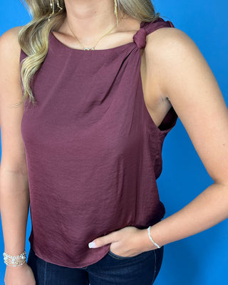 Wine sleeveless top with a soft draped silhouette, rounded neckline, and chic knotted shoulder detail.