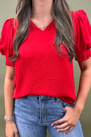 Red puff sleeve blouse with v-neckline styled with light wash wide leg frayed hem jeans and gold loafers.