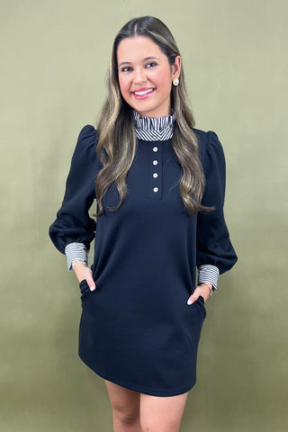 Woman wearing a navy blue dress with striped cuffs and collar against a green background