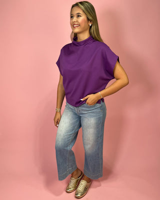 Woman wearing a purple top and blue jeans against a pink background