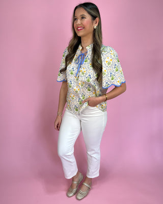Woman wearing a floral blouse and white pants against a pink background