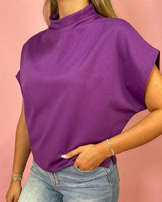 Purple sleeveless top worn by a person on a pink background