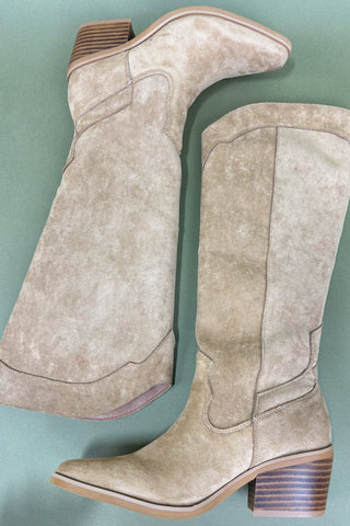 Pair of beige suede boots on a light blue background