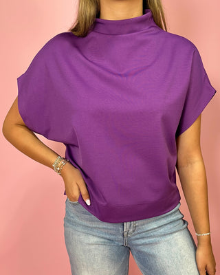 Person wearing a purple top and light blue jeans against a pink background