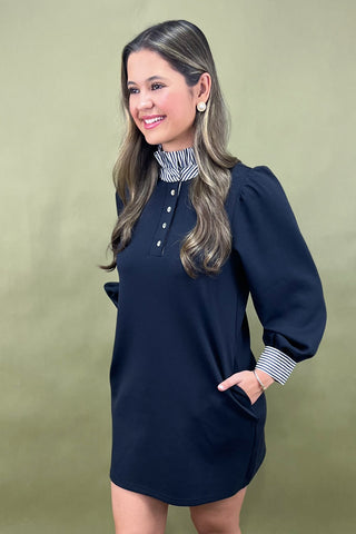 Woman wearing a navy dress with a striped collar against a green background